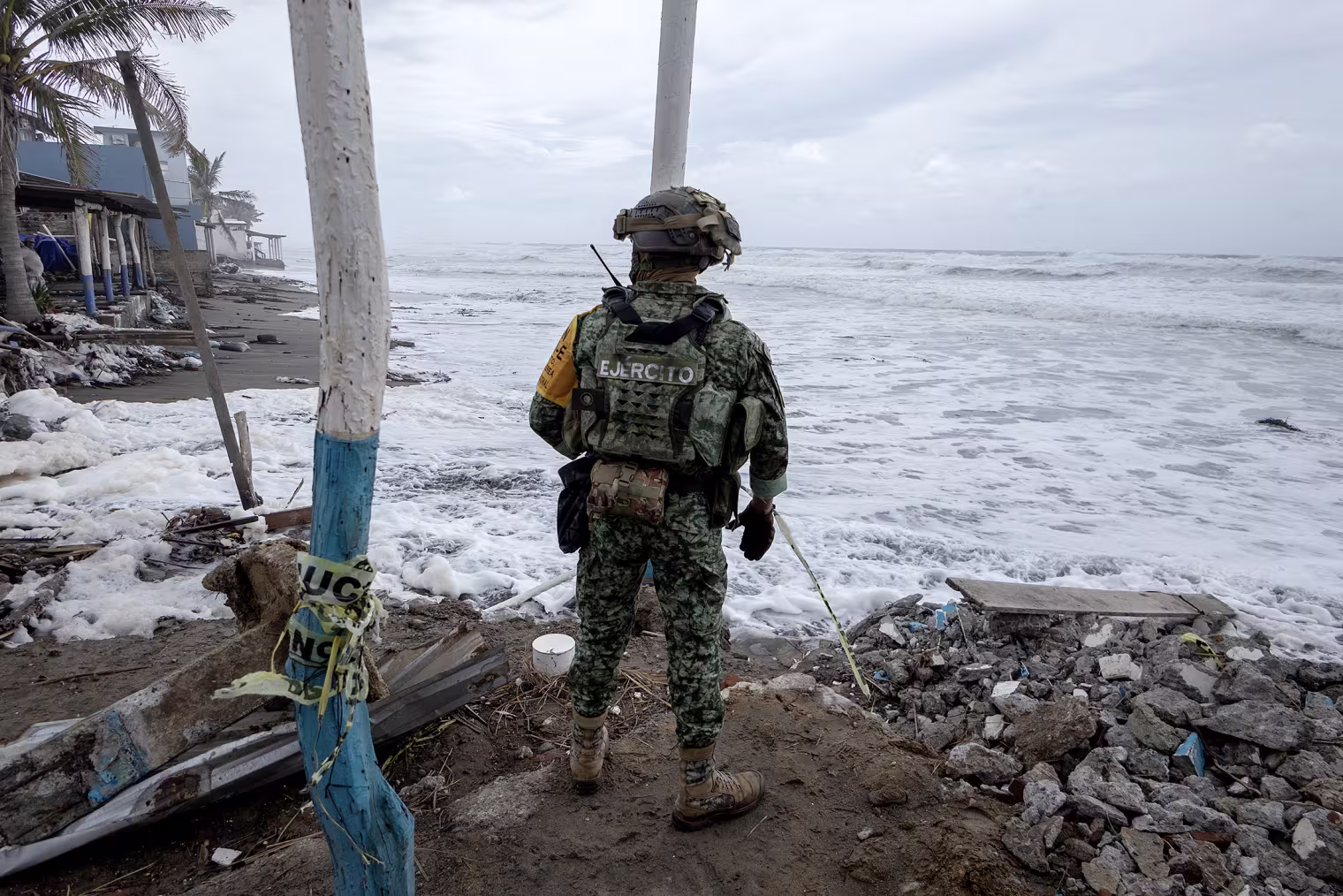 A soldier wearing camouflage fatigues and a helmet surveys whitecap waves on a beach.