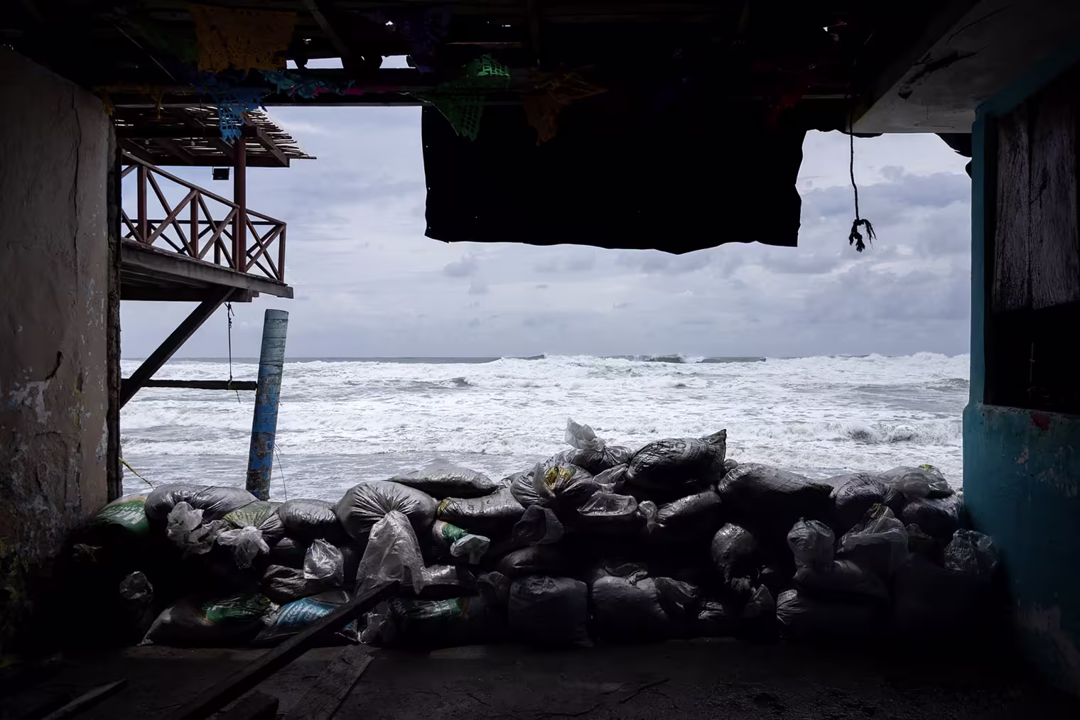 Waves are visible through an opening in a building, with sandbags stacked on the ground.