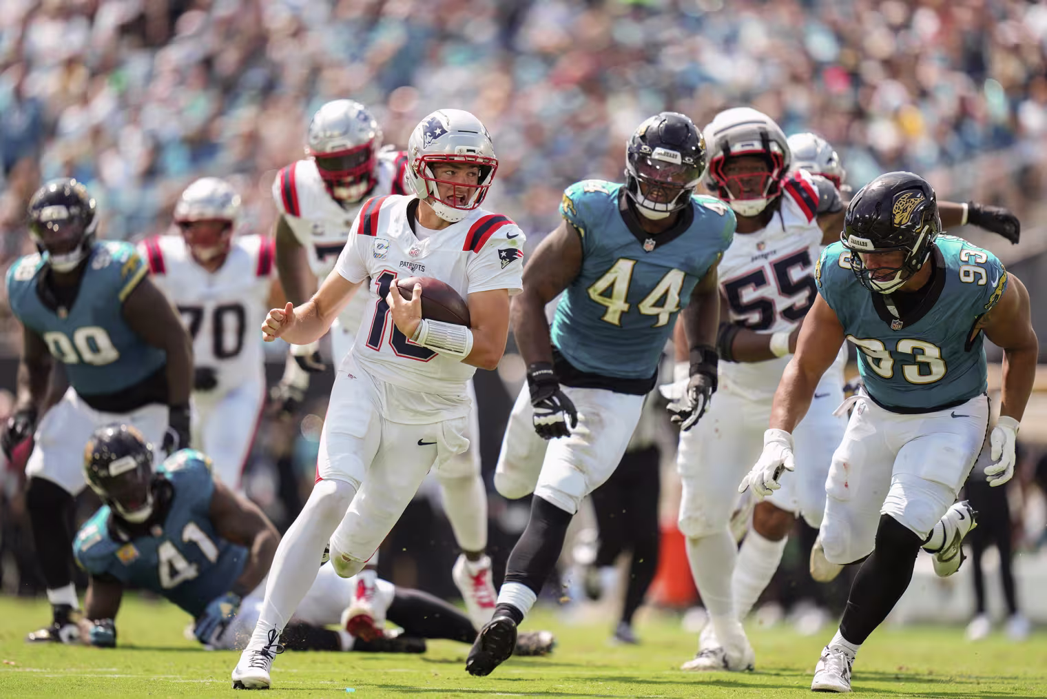 Drake Maye running the football in front of several Jaguar defenders. 