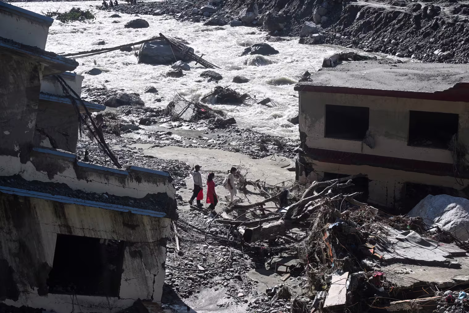 People walk past damaged houses.