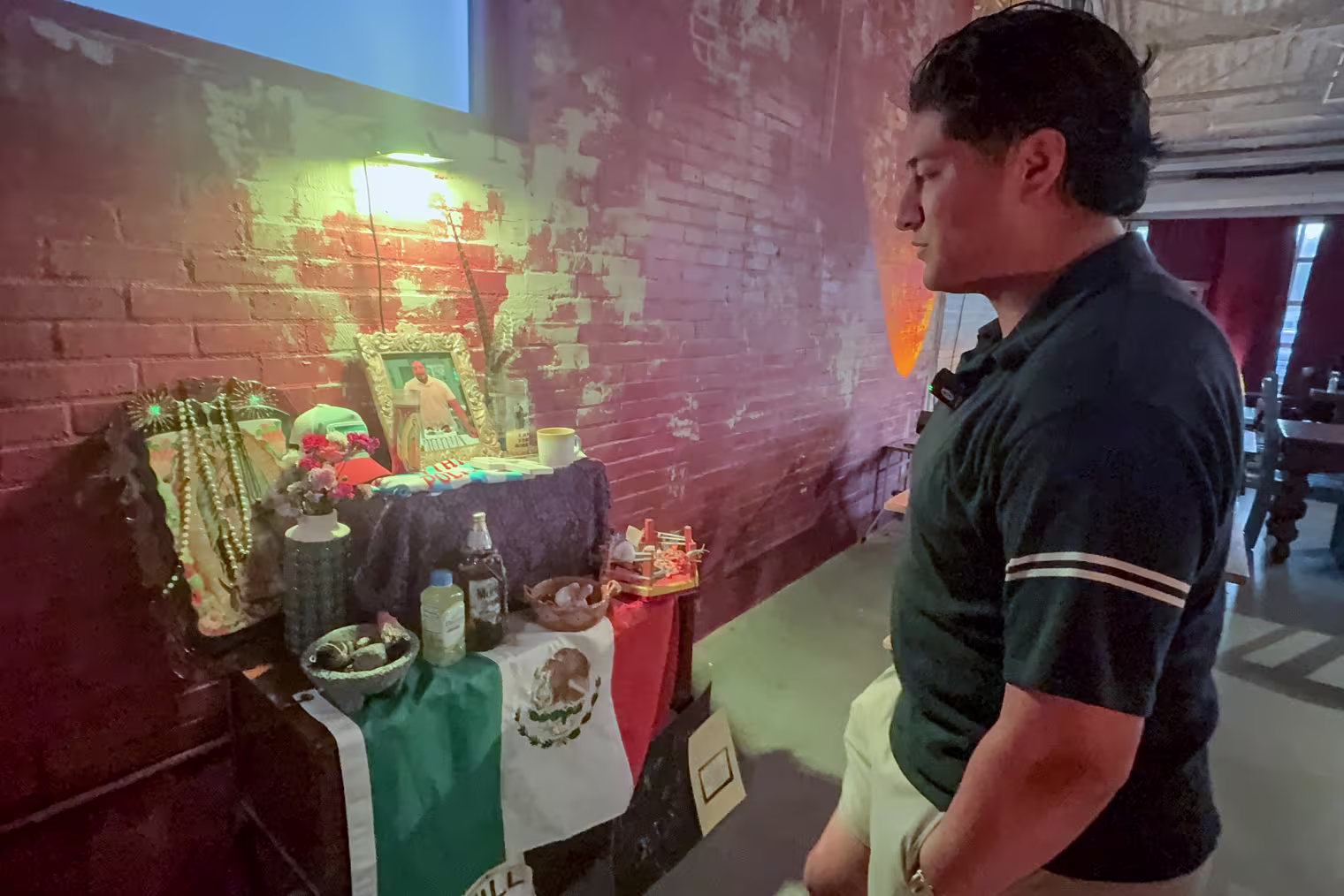 A man standing in front of an altar bearing a Mexican flag.