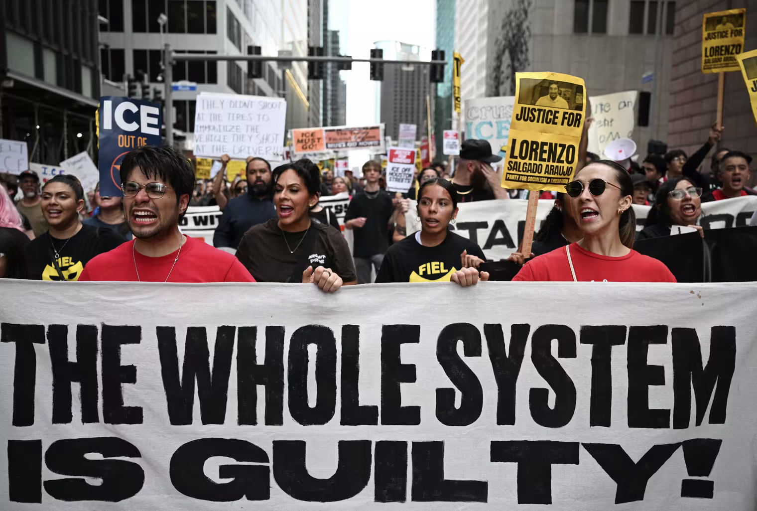 Protestors holding a large white banner reading THE WHOLE SYSTEM IS GUILTY!