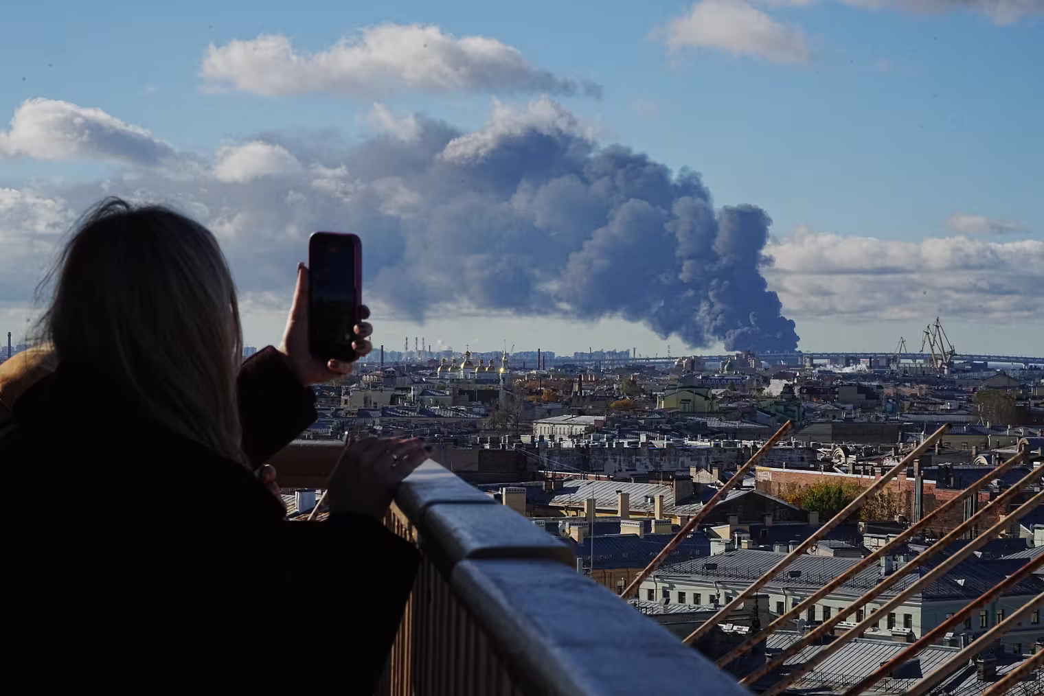 Image: A woman on a rooftop takes a photo of smoke billowing over the skyline.