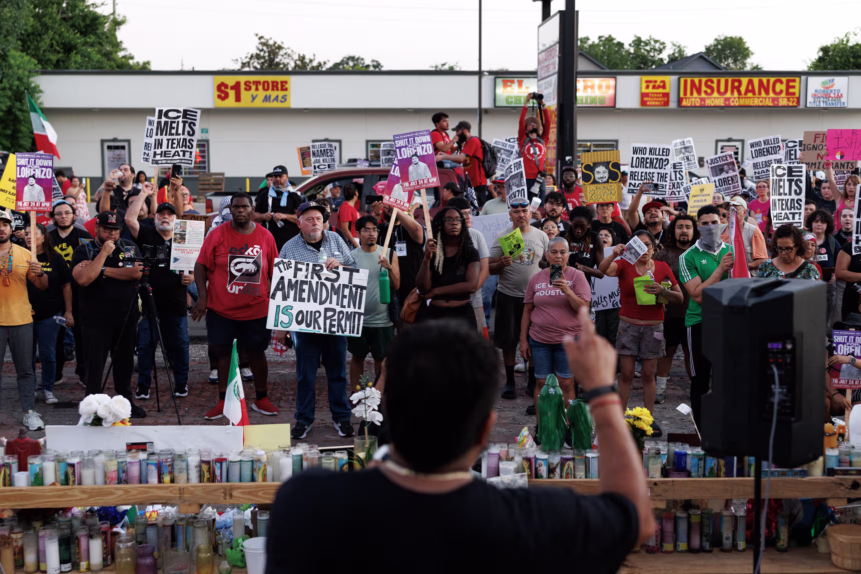 A large crowd gathered and holiding signs in front of a makeshift memorial. 