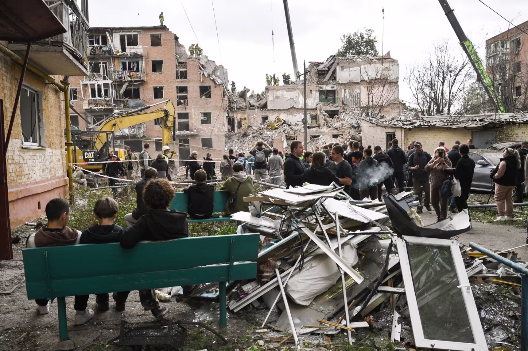 Local residents look at rescuers working on a multi-floor residential building destroyed among rubble