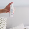 Hand spraying the Deep Sleep Pillow Spray on a pillow on a bed