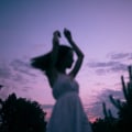 silhouette of young woman dancing in white dress under the sunset looking away