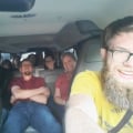 A group of people sit inside a van with gray seats.
