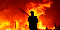 A utility worker uses a hose to extinguish fire near power poles as the Dixie Fire moves through the area on Aug. 16, 2021, near Janesville, Calif.