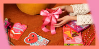 Hands holding a red box with a pink ribbon