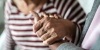 Nurse or home caregiver and senior woman holding hands at home