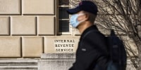 A man wearing a mask rides a scooter past the Internal Revenue Service headquarters