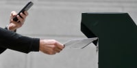 A man photographs himself depositing his ballot in an official ballot drop box while a long line of voters queue outside of Philadelphia City Hall at the satellite polling station in Philadelphia, on Oct. 27, 2020.