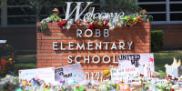 Bouquets of flowers are set in front of the Robb Elementary school brick signage