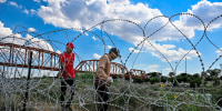 Migrants walk along concertina wire near the border with Mexico