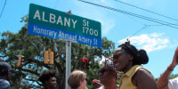 Wanda Cooper-Jones, center in yellow dress, poses for photos with supporters beneath a new street sign honoring her son, Ahmaud Arbery, at the unveiling on Aug. 9, 2022, in Brunswick, Ga.