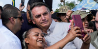 Brazilian President Jair Bolsonaro takes a photo with a supporter as he campaigns for reelection in Brasilia, on Oct. 24, 2022.
