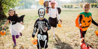 Multi ethnic group of children go for trick or treat, they running in park and wear costumes. Dog in costume is with them too