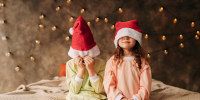 Happy funny little kids teens a boy and a girl in pajamas and Santa Claus hats are getting involved hugging and fooling around sitting on the bed in a cozy bedroom at home during the Christmas holidays
