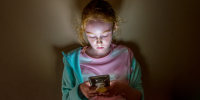 Young girl looking into mobile phone screen, in dark room.