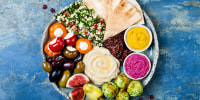 Middle Eastern meze platter with green falafel, pita, sun dried tomatoes, pumpkin and beet hummus, olives, stuffed peppers, tabbouleh, figs.