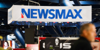 Signage for the Newsmax conservative television broadcasting network is displayed at a broadcast TV booth at the National Rifle Association (NRA) annual meeting at the George R. Brown Convention Center, in Houston, Texas on May 28, 2022. 