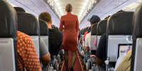 Female cabin crew walks away down aircraft cabin isle