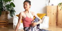Young Asian woman doing seated spinal twist at home living room.