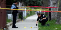 A Chicago Police officer watches as a evidence technician officer investigates a gun at a crime scene in Chicago