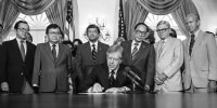 President Jimmy Carter signs a bill at the White House creating a commission to look into the wartime internment of Japanese Americans as Senator Daniel Inouye, D-Hawaii, Rep. Norm Mineta, D-Calif., Senator Spark Matsunaga, D-Hawaii, Rep. George Danielson, D-Calif., watch, on July 31, 1980.