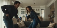 A young couple holding cans of Bud Light dances in a living room.