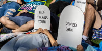 Protesters lie on the ground holding cardboard signs shaped like tombstones in front of the Marriott Fort Lauderdale Airport as the Florida Board of Medicine meets inside.