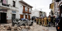 Rescue workers stand next to a car crushed by debris after an earthquake