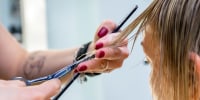 Hands of a professional hairdresser scissors the bangs of wet hair of a blonde woman.