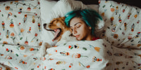 High Angle View Of Woman Sleeping With Dog On Bed