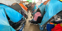 Teresa Muñoz, seated at center wearing a pink hoodie, rests at a tent at a migrant shelter where she has been trying unsuccessfully for about a month to get an appointment to enter the United States through a new U.S. government mobile phone app in Tijuana, Mexico, Thursday, May 11, 2023. She fled her home in the Mexican state of Michoacan after her husband was killed and she was badly beaten. (AP Photo/Elliot Spagat)
