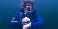 In this photo provided by the Florida Keys News Bureau, diving explorer and medical researcher Dr. Joseph Dituri points to his watch Friday, June 9, 2023, indicating that it is time to surface after spending 100 days in the Jules' Undersea Lodge marine habitat at the bottom of a Key Largo, Fla., lagoon. Dituri broke the previous 73-day record for underwater human habitation at ambient pressure, undertook medical and marine science research and interacted online with more than 5,500 students during his Project Neptune 100 mission organized by the Marine Resources Development Foundation. (Mariano Lorde/Florida Keys News Bureau via AP)