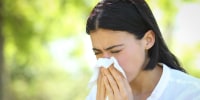 Ill woman sneezing covering mouth with a wipe in a park