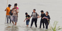Migrants who crossed the Rio Grande from Mexico walk past large buoys being deployed as a border barrier in Eagle Pass, Texas, on July 12, 2023.