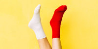 woman legs in the air with a red sock on one foot and a white sock on the other foot on yellow background