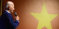 Joe Biden holding microphone in front of Vietnam's flag. 