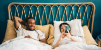 Smiling girlfriend sharing smart phone with boyfriend while lying on bed