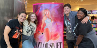 A group of young people pose in front of a Taylor Swift poster