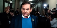 Rep. George Santos walks in a Capitol hallway surrounded by journalists and camera crews