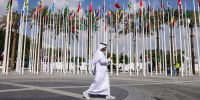 Image: A man walks past flags of nations participating in the UNFCCC COP28 Climate Conference
