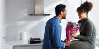 Romantic couple at home with man surprising woman with bunch of flowers celebrating valentines day, birthday or anniversary