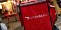 A door-dash delivery driver waits near a restaurant.