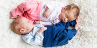 Newborn twins sleeping on white blanket