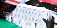 A person holds a stack of ballots at a computer desk