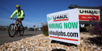A cyclist rides by a now hiring sign posted in front of a U-Haul rental center in San Rafael, Calif.